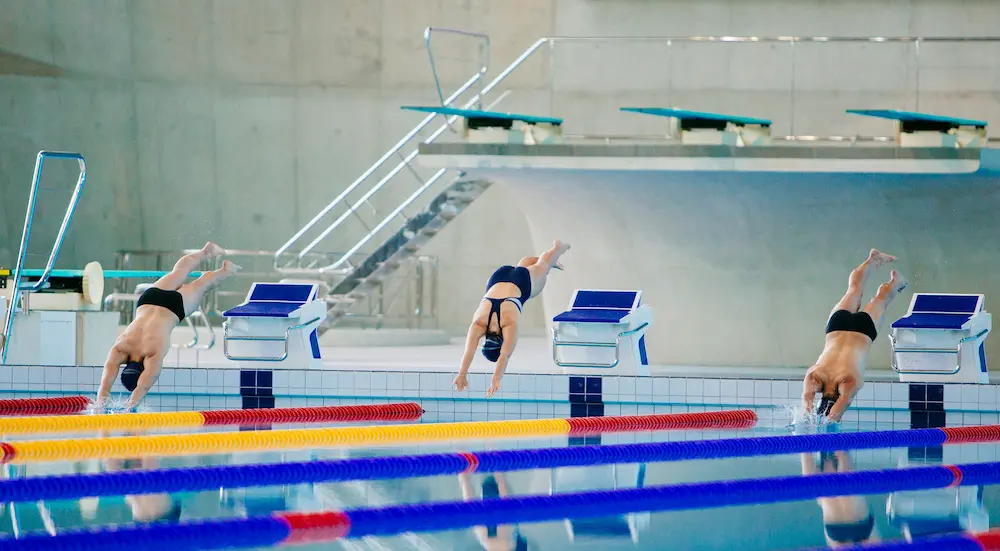 Masters swimmer standing behind the blocks at a competition pool, adjusting goggles before a race